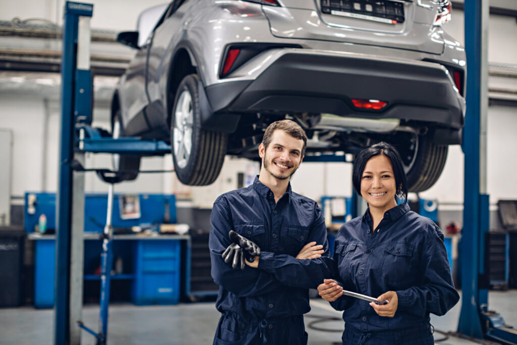 auto-car-repair-service-center-two-happy-mechanics-man-woman-standing-by-car